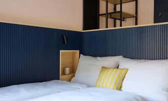 A modern bedroom with a blue wall design and cozy beds. The room is minimalist and well-lit.