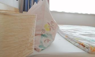 A cozy bedroom with a bed and a bedside table. The windows let in plenty of daylight.