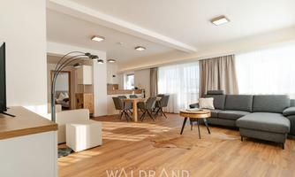 Modern apartment with plenty of daylight and wooden floors. A cozy sofa, a dining table, and an open kitchen create an inviting atmosphere.