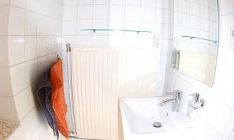 A small bathroom with white tiles and a sink. There is a towel and an orange carpet on the floor.