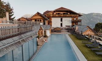 A beautiful hotel with traditional wooden architecture and an outdoor pool. The surroundings are surrounded by mountains and invite relaxation.