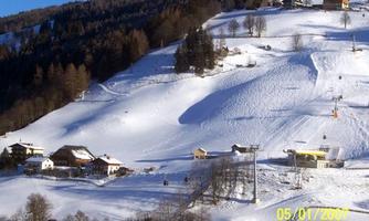 A snowy winter landscape with a ski slope and several cabins. In the background, there are trees and a blue sky.
