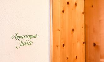 A wooden door to an apartment named "Julia". The wall next to it is in a soft color and has the inscription.