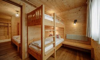 A cozy children's room with a bunk bed and a single bed. The room is made of wood and provides a warm, inviting atmosphere.