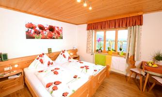 A cozy bedroom with a large double bed and colorful bed covers. The walls are light, and there are windows with a view of nature.
