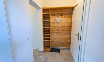 A bright entrance area with a wooden shelf and a heart made of wood. Coat hooks for coats and bags hang on the wall.