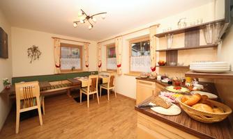A cozy kitchen with a dining table and chairs. Fresh bread and pastries are laid out on the sideboard, ready for the meal.