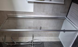A modern shower with transparent glass doors and an elegant faucet. The floor is tiled, and the space feels bright and inviting.