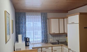 A bright kitchen with a table and chairs. There are modern kitchen cabinets and windows with curtains.