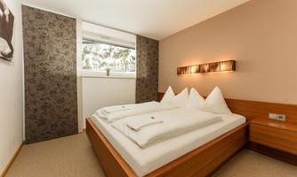 A cozy bedroom with a double bed and modern wooden paneling. Daylight enters the room through the window.