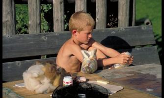 A small boy is sitting on a wooden bench and is occupied with wool fibers. Next to him are various materials as he works intently.