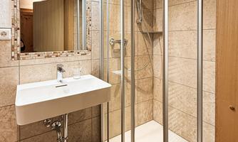 A modern bathroom with a shower and a sink. The walls are tiled and there is a mirror above the sink.