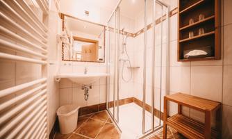 A modern bathroom with a shower and a sink. The walls are brightly tiled and there is a wooden bench as well as a towel holder.