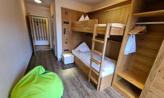 A small room with a bunk bed and a cozy bean bag. The walls are made of wood and the floor is made of laminate wood.