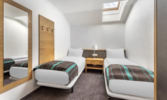 A simple room with two single beds and modern furniture. The room has a window with light and a mirror on the wall.