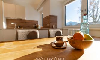 A cozy table with a bowl of fresh apples and a coffee cup. In the background, there is a modern kitchen and a beautiful view of the mountains through the window.