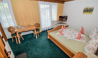 A cozy bedroom with a double bed, a table, and chairs. Large windows let in plenty of light and create a pleasant atmosphere.