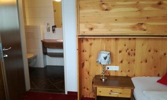 A cozy room with wooden walls and a nightstand. The bathroom is visible in the background.