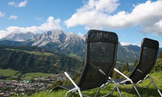 Two loungers are placed on a meadow with a view of the mountains. The sky is blue and partly covered with some clouds.