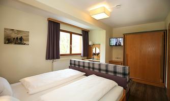A cozy bedroom with two blankets and a television. The room has large windows and wooden furniture.