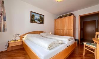 A cozy bedroom with a double bed and wooden floor. A picture hangs on the wall, and a wardrobe stands in the room.