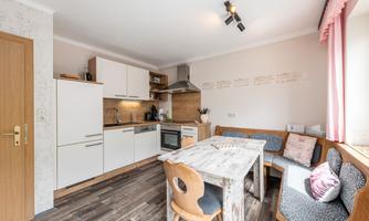 A modern kitchen with white cabinets and wooden details. A dining table with comfortable seating invites you to linger.