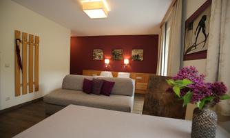 A cozy room with a modern sofa and colorful cushions. Pictures are hanging on the wall, and a bouquet of flowers is on the table.