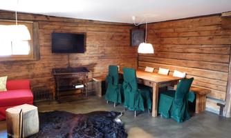 A cozy living space with wooden walls and a red couch. A dining table with green chairs and a TV on the wall.