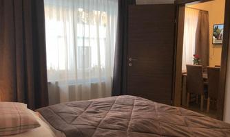 A cozy bedroom with a bed and a large window. In the background, there is a dining area with a table and chairs.