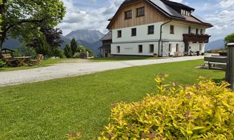 A beautiful house in a rural setting with a green lawn and mountains in the background. The sky is partly cloudy and invites a relaxed stay.