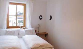 A bright bedroom with a large bed and white pillows. The window offers a view outside and there is a small lamp on the nightstand.