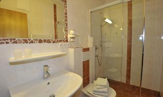 A modern bathroom with a shower and clean towels. The walls are brightly tiled and there is a large mirror above the sink.