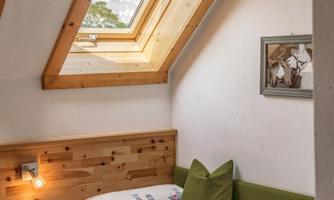 A cozy room in the attic with a window and wood paneling. A colorful blanket and a pillow are on the bed.