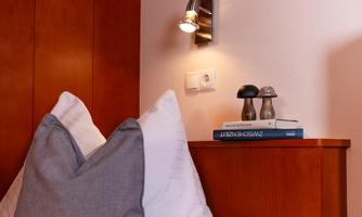 A cozy bedroom with a wooden nightstand. On the table, there are books and a decorative lamp.