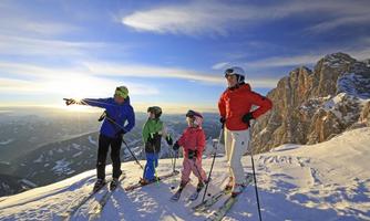 A family stands on a snow-covered mountain and enjoys the view. They are wearing ski gear and looking into the distance.