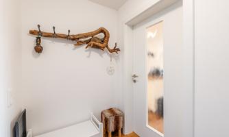 A bright entrance area with a wooden shelf and several hooks. On the right, there is a door with glass insert.