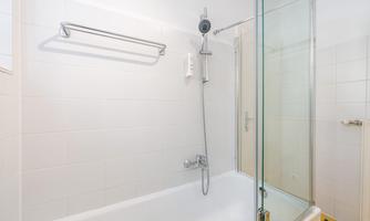 A modern bathroom with a bathtub and a shower cabin. The walls are bright and clean, with a minimalist design.
