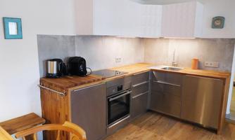 A modern kitchen with wood and stainless steel surfaces. It features a refrigerator, oven, and cooktop, as well as a bright, friendly atmosphere.
