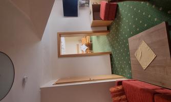 A cozy living area with a red sofa and a table. In the background, there are additional rooms and a television visible.