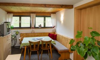 A cozy room with a wooden chair set and a large table. 

Large windows let in plenty of light, and the room is decorated with plants.