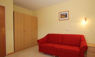 A bright room with yellow walls and a red sofa. The room contains a wardrobe and a picture on the wall.