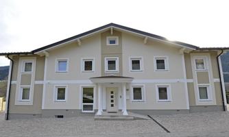 A modern two-story residential building with a bright exterior paint. The facade is symmetrically designed and has several windows.