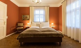 A cozy bedroom with a large bed and soft colors. The walls are painted in a warm red tone, and there are numerous windows that provide natural light.