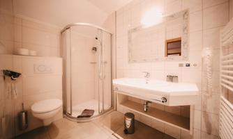 A modern bathroom with a shower, a sink, and a toilet. The walls are brightly tiled, and there is a mirror above the sink.