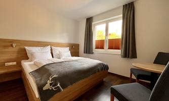 A cozy room with a double bed and light wood. There is a small table and chairs as well as a window with a view.