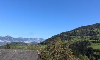 A beautiful mountain landscape with green hills and a clear blue sky. In the foreground, a roof can be seen that complements the rural environment.