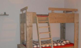A wooden loft bed with red bedding and a ladder. The room has a simple, modern style with a pendant lamp.