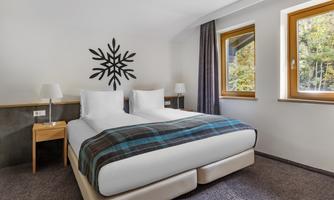 A modern bedroom with two beds and a cozy carpet. Large windows provide plenty of daylight and a pleasant atmosphere.