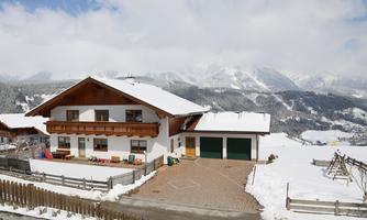 A cozy house in the snow with mountains in the background. The sky is cloudy and the landscape is wintry and calm.