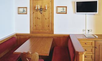 A cozy dining area with a wooden table and red upholstered benches. A television and traditional pictures hang on the wall.